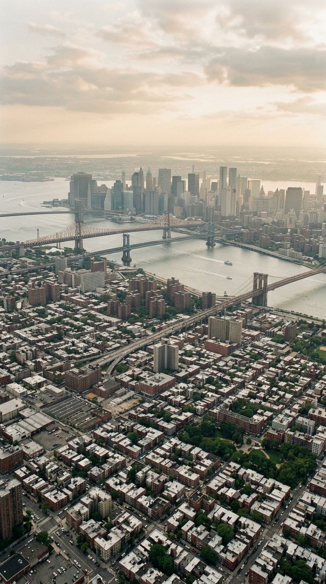 Aerial New York City boroughs at golden hour with East River bridges.